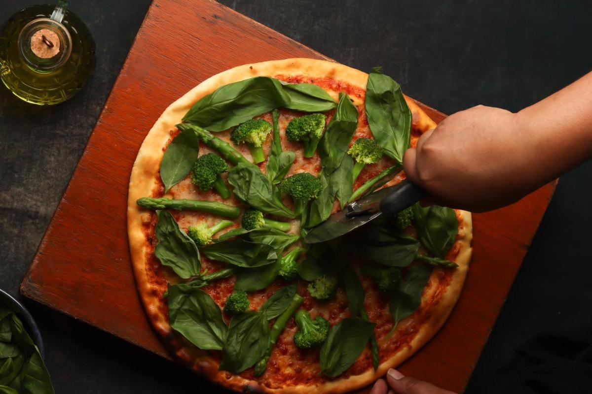 a person cutting a pizza with a pizza cutter at Hyatt Hyderabad Gachibowli in Hyderabad