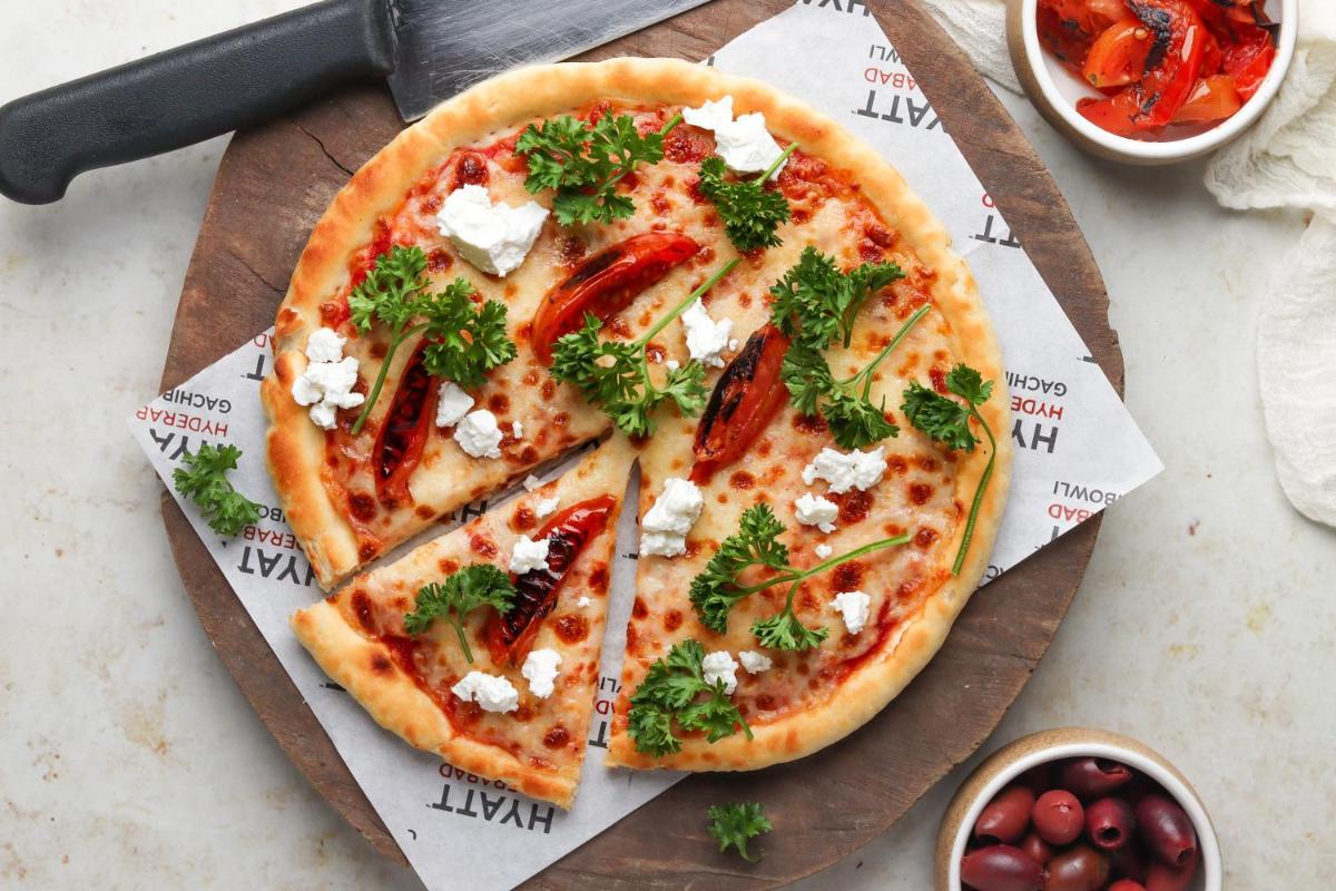 a pizza sitting on top of a wooden cutting board at Hyatt Hyderabad Gachibowli in Hyderabad