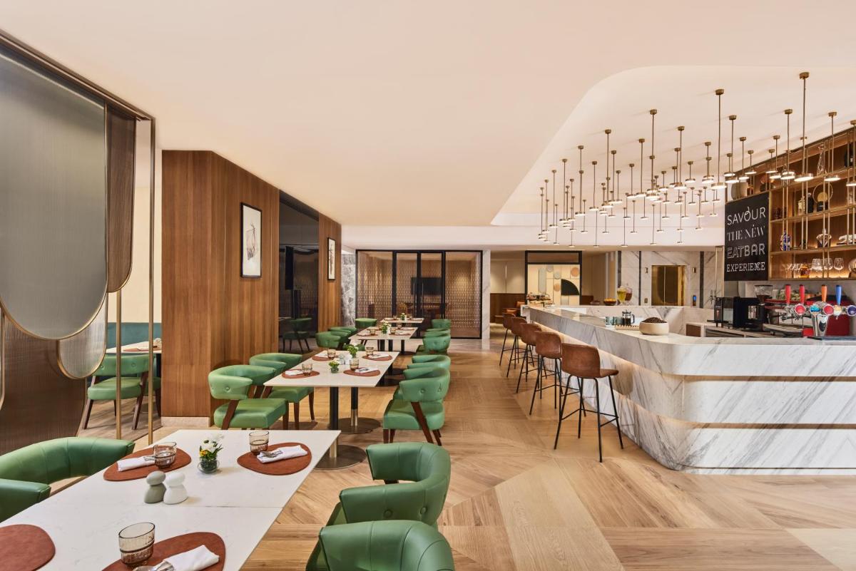 a restaurant with tables and green chairs and a bar at Novotel Mumbai International Airport in Mumbai
