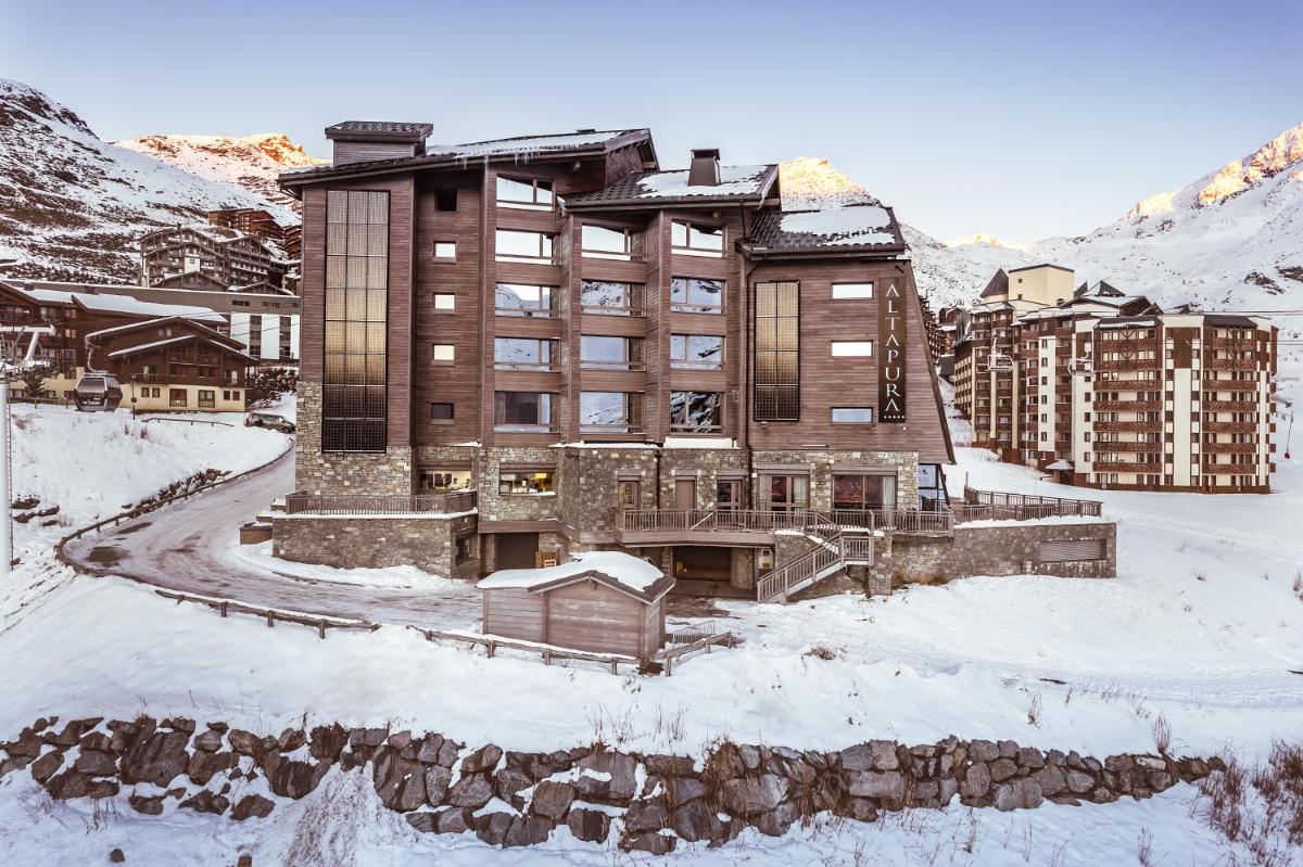un grand bâtiment dans la neige avec des montagnes en arrière-plan dans l'établissement Altapura Hôtel & Spa Val Thorens, à Val Thorens