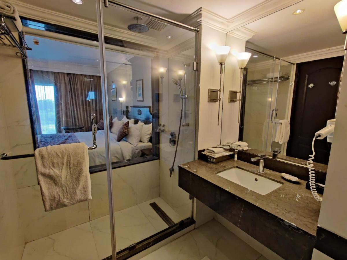 a bathroom with a shower and a sink and a bed at Hotel Royal Orchid Bangalore in Bengaluru