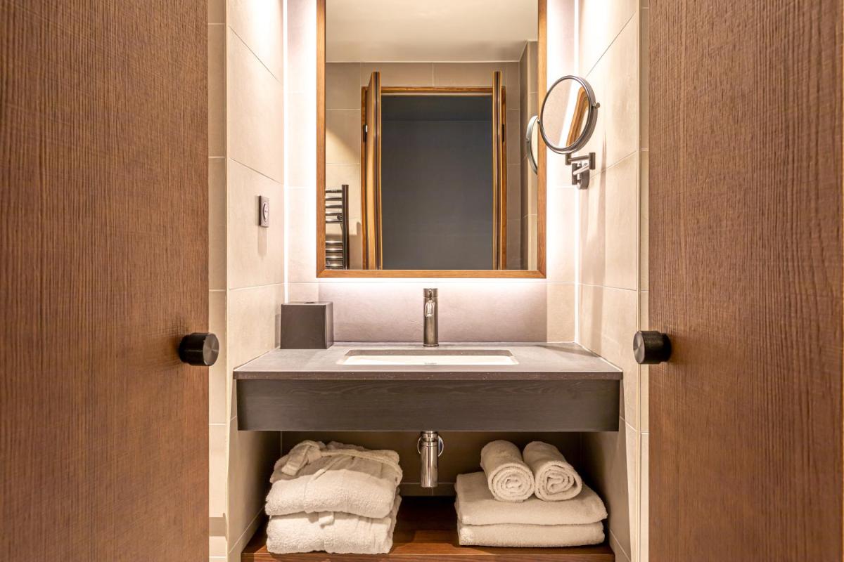 une salle de bain avec un lavabo, un miroir et des serviettes dans l'établissement Le Bellune Paris, à Paris
