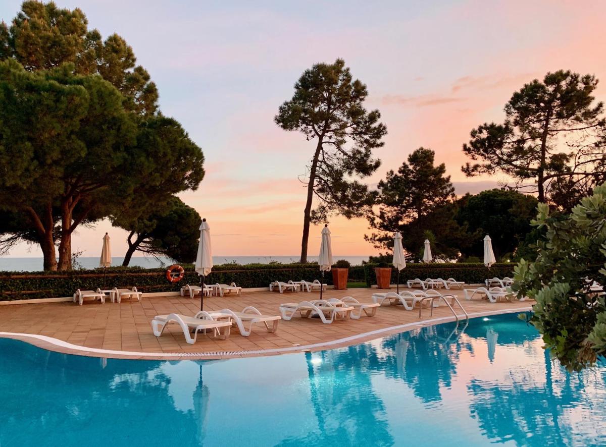 uma piscina com cadeiras brancas e um resort em PortoBay Falesia em Albufeira