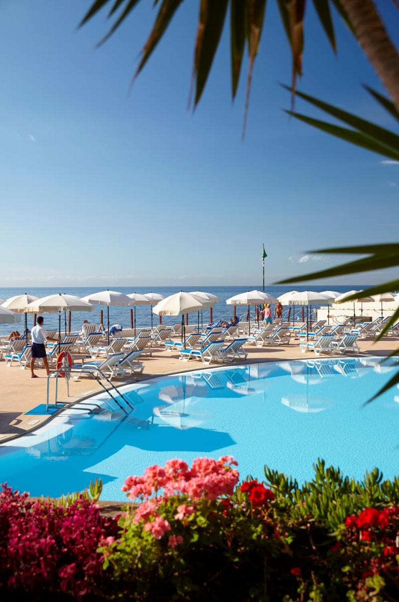 uma piscina com cadeiras e guarda-sóis na praia em The Cliff Bay - PortoBay no Funchal