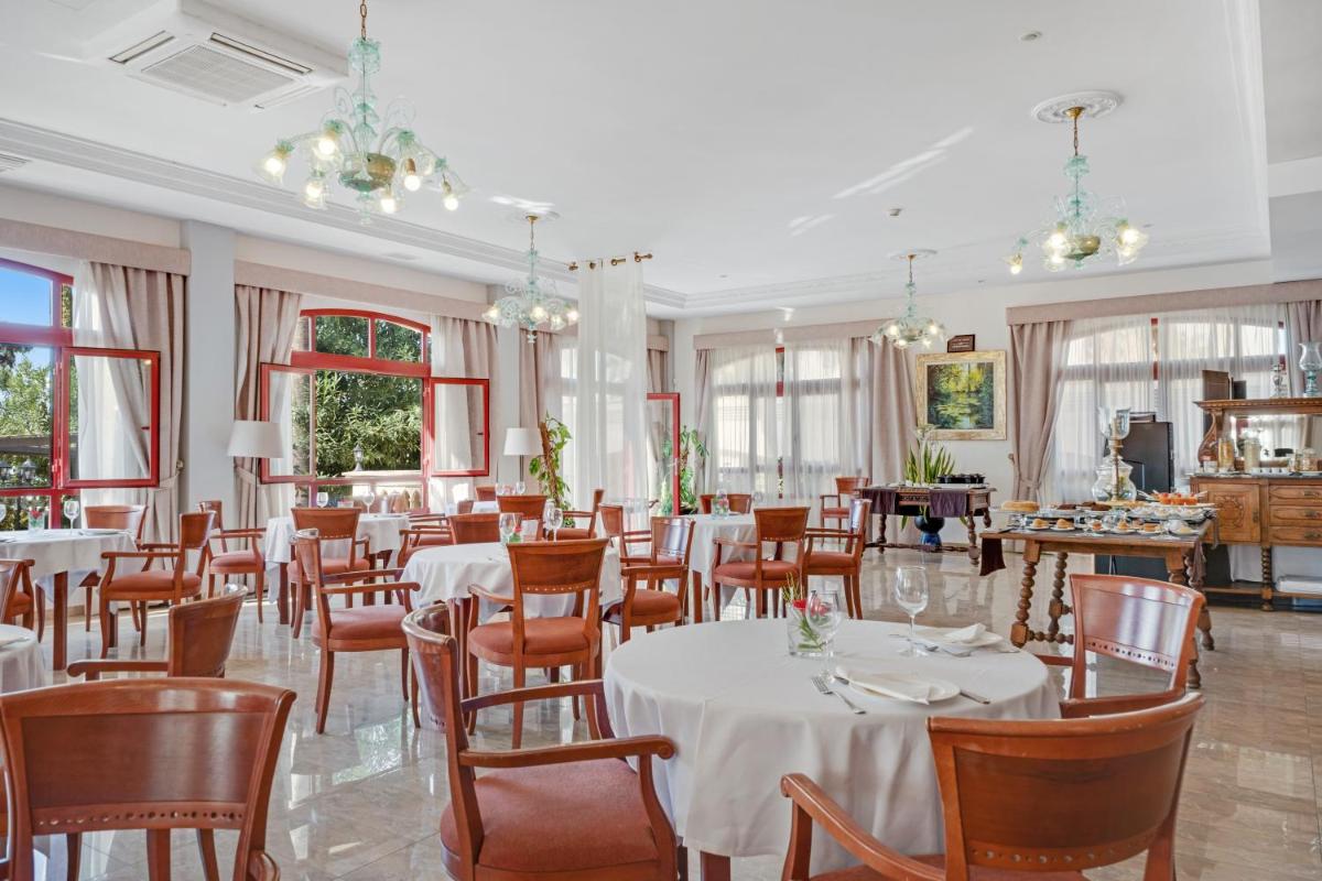Un restaurante con mesas y sillas blancas y ventanas. en Hotel Ciutat Jardi, en Palma de Mallorca