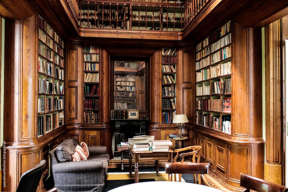 uma biblioteca com estantes de madeira e uma pessoa sentada em uma cadeira em Hotel Quinta das Lagrimas - Small Luxury Hotels em Coimbra