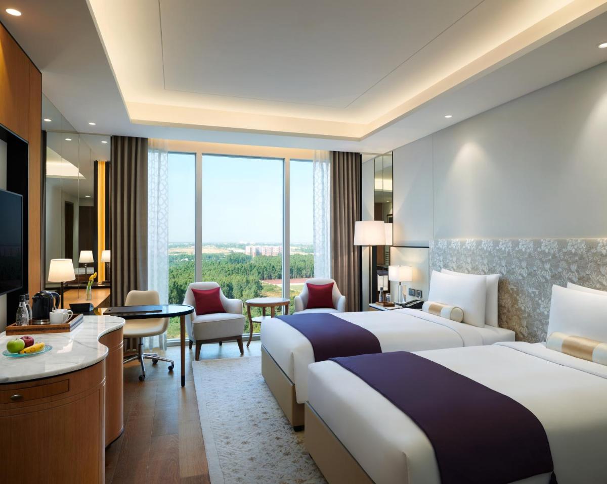 a hotel room with two beds and a desk at The Leela Bhartiya City Bengaluru in Bengaluru a hotel room with two beds and a desk at The Leela Bhartiya City Bengaluru in Bengaluru