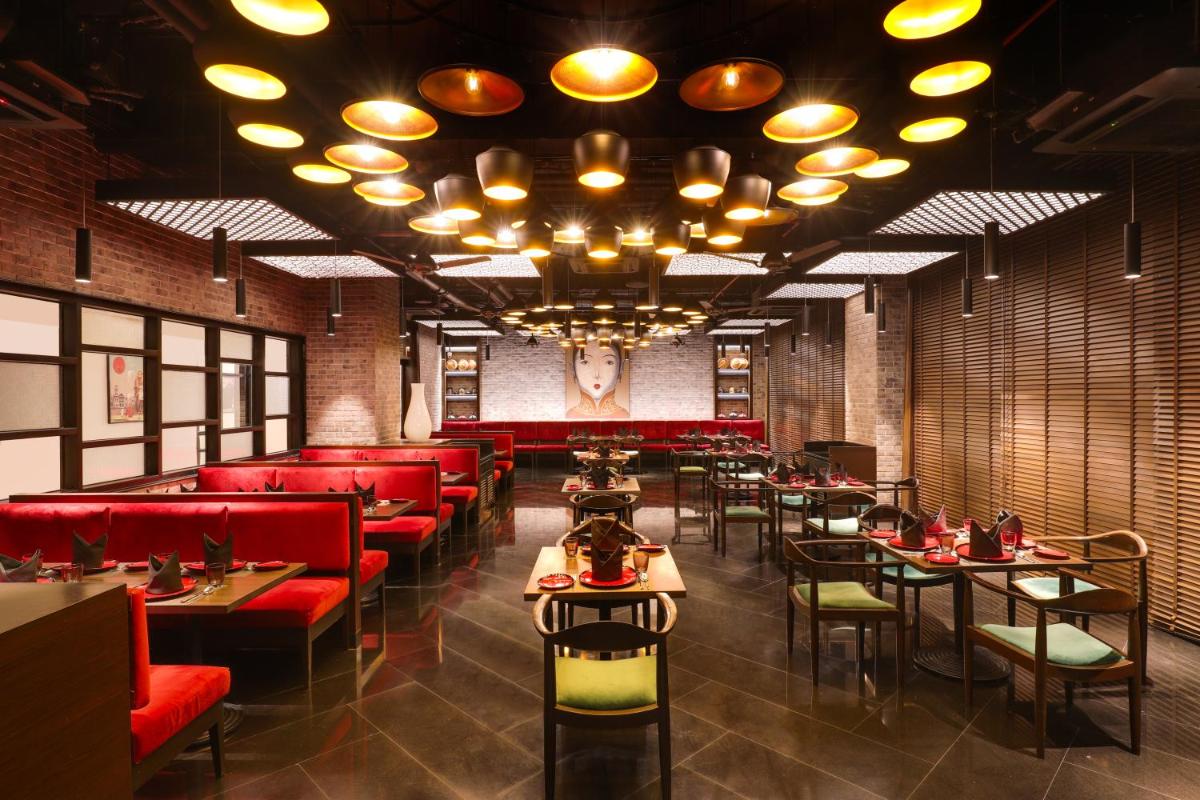 a restaurant with red seats and tables and a chandelier at Lemon Tree Premier, Mumbai International Airport in Mumbai