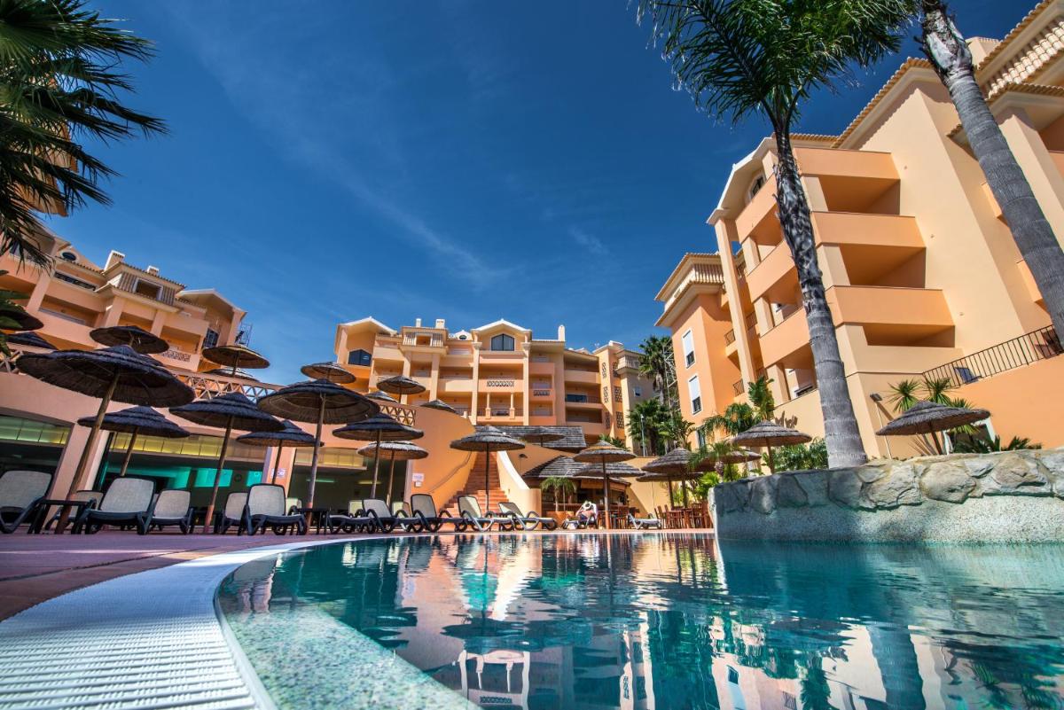 uma piscina com guarda-sóis, cadeiras e edifícios em Estrela da Luz Resort na Praia da Luz