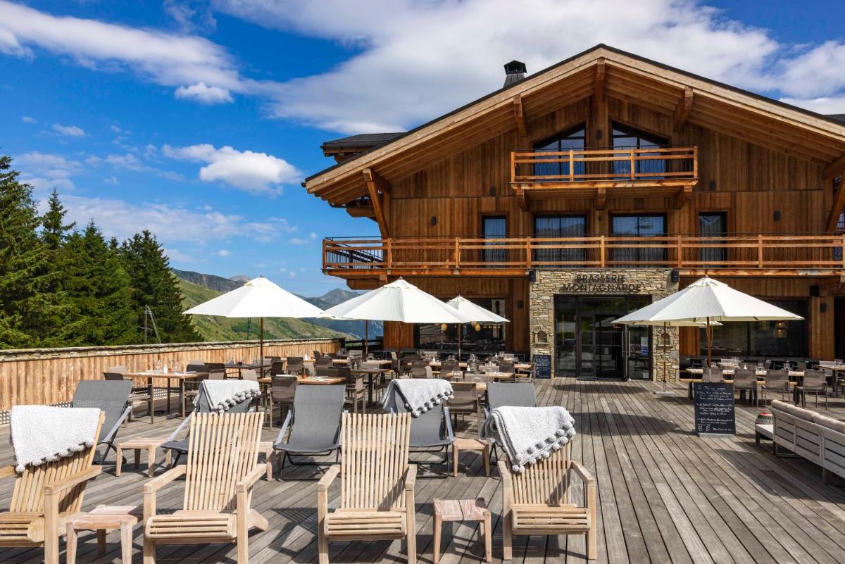 une terrasse avec des chaises et des parasols en face d'un bâtiment dans l'établissement HIGALIK HOTEL, aux Menuires
