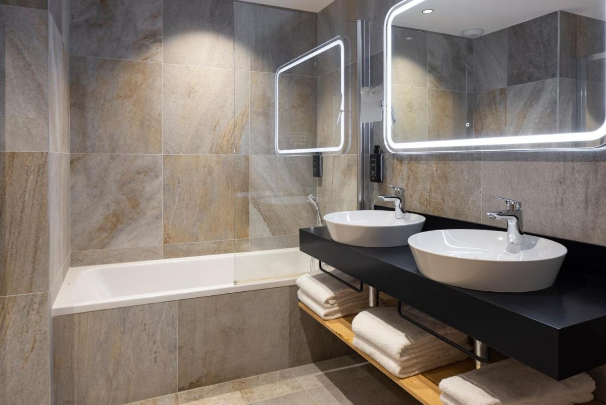 une salle de bain avec deux lavabos, une baignoire et un miroir dans l'établissement HIGALIK HOTEL, aux Menuires