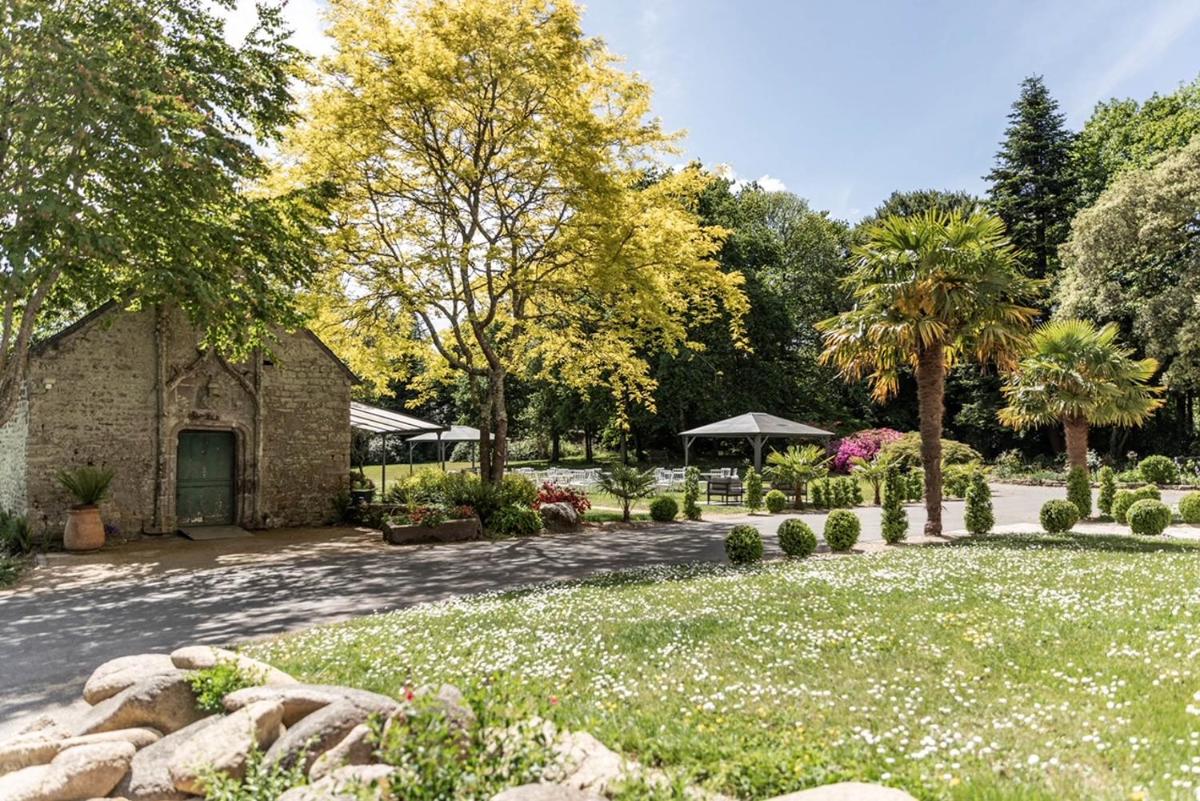 un jardin avec un bâtiment en pierre et des arbres dans l'établissement Manoir des Indes, The Originals Relais, à Quimper 29 autres photos