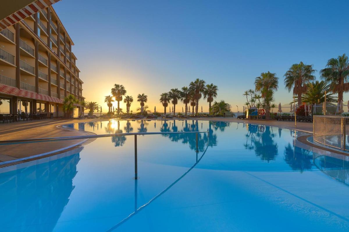 uma grande piscina com palmeiras e um edifício em The Views Oasis no Caniço