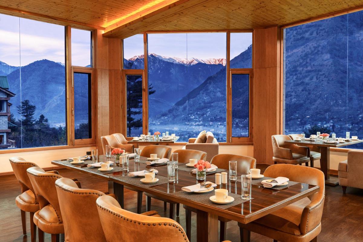 a restaurant with tables and chairs and a view of mountains at Baragarh Resort & Spa, Manali- IHCL SeleQtions in Manāli
