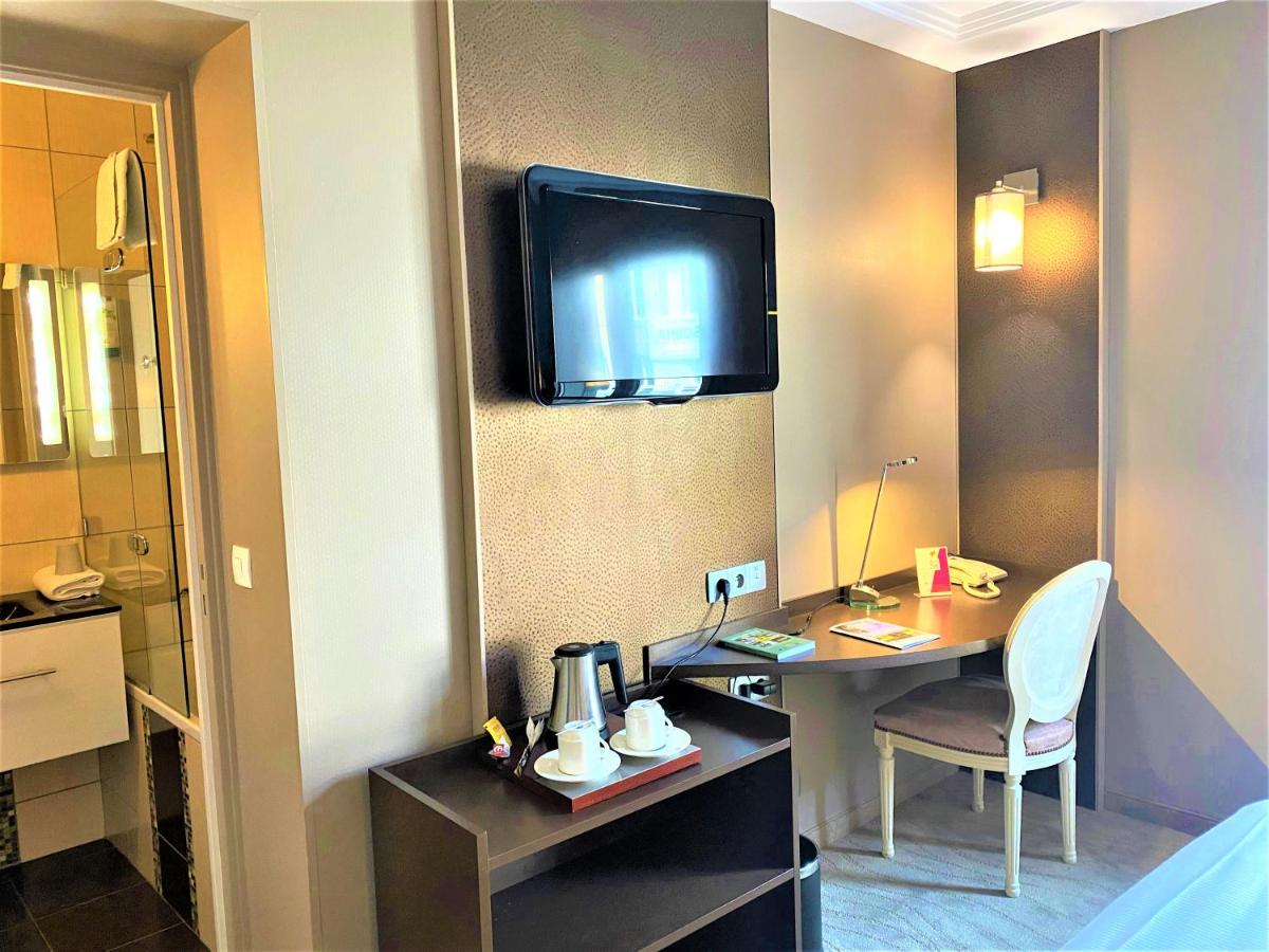 une chambre d'hôtel avec un bureau et une télévision au mur dans l'établissement Logis Hôtel Restaurant Le Fruitier, à Villedieu-les-Poêles