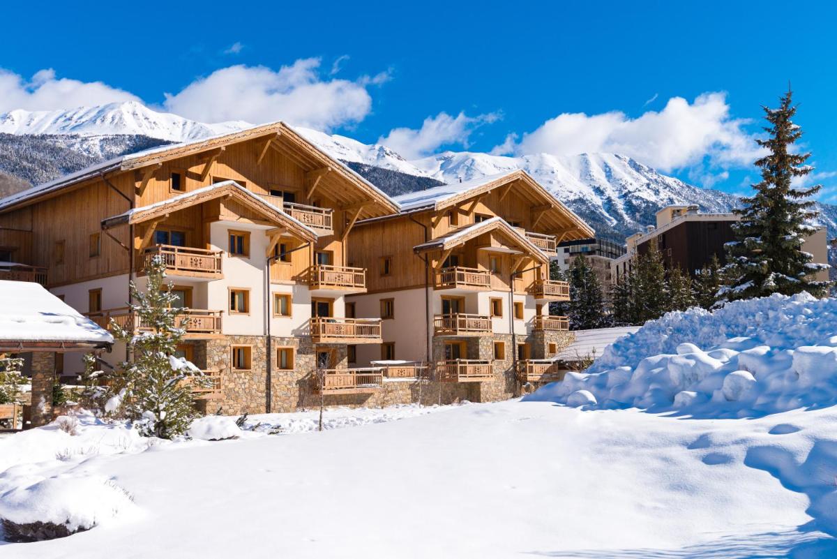 un lodge dans la neige avec des montagnes en arrière-plan dans l'établissement Lagrange Vacances Le Hameau du Rocher Blanc, à Saint-Chaffrey