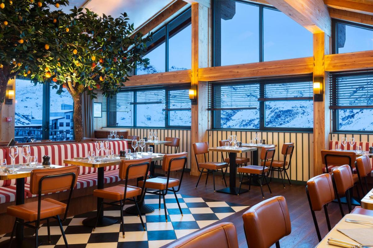 un restaurant avec des tables, des chaises et des fenêtres dans l'établissement Ours Blanc Hotel & Spa, aux Menuires