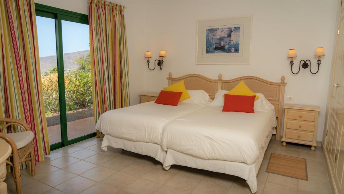 Un dormitorio con una cama blanca con almohadas rojas y amarillas en La Palma Jardín Resort, en El Paso