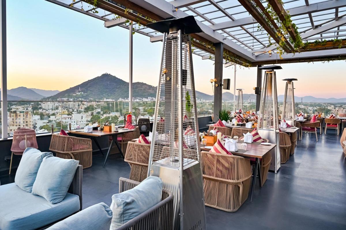 a restaurant with tables and chairs and mountains in the background at Parallel Hotel Udaipur, a member of Radisson Individuals in Udaipur