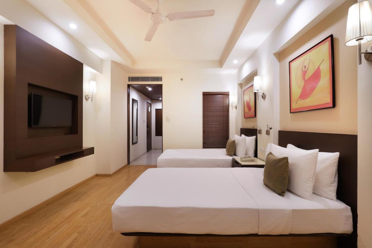 a bedroom with two beds and a flat screen tv at Lemon Tree Premier, Ulsoor Lake, Bengaluru in Bengaluru