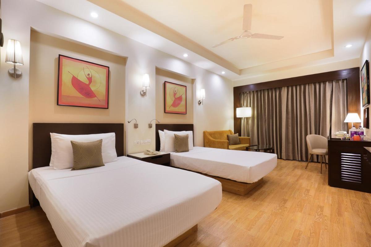 a hotel room with two beds and a desk at Lemon Tree Premier, Ulsoor Lake, Bengaluru in Bengaluru