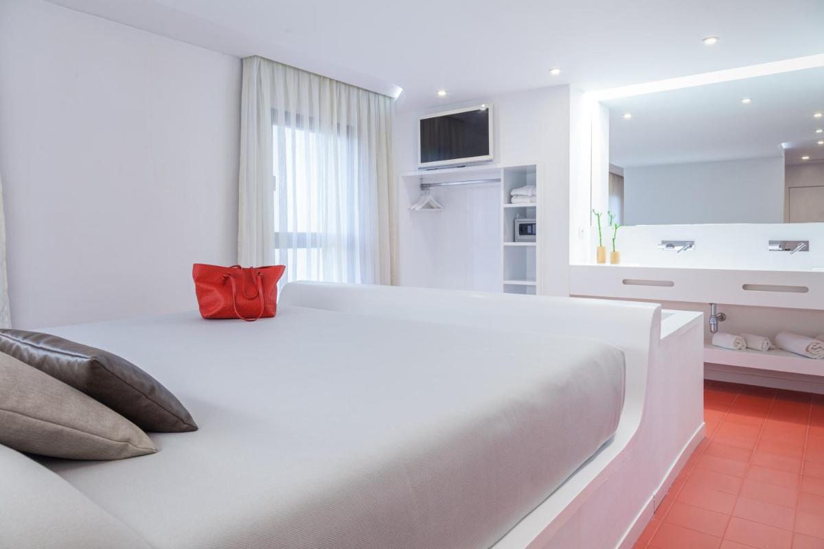 Dormitorio blanco con cama blanca grande y almohada roja en Hotel Maciá Granada Five Senses Rooms & Suites, en Granada