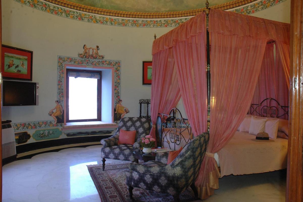 a bedroom with a bed and a chair and a window at Shiv Niwas Palace by HRH Group of Hotels in Udaipur
