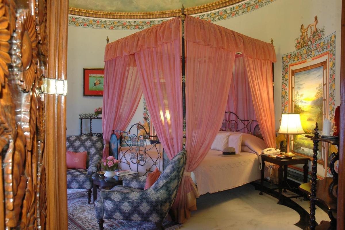 a bedroom with a canopy bed with two chairs at Shiv Niwas Palace by HRH Group of Hotels in Udaipur