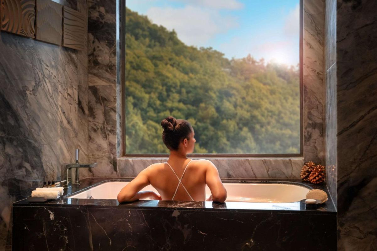 a woman sitting in a bath tub looking out a window at Hyatt Regency Dehradun Resort and Spa in Dehradun