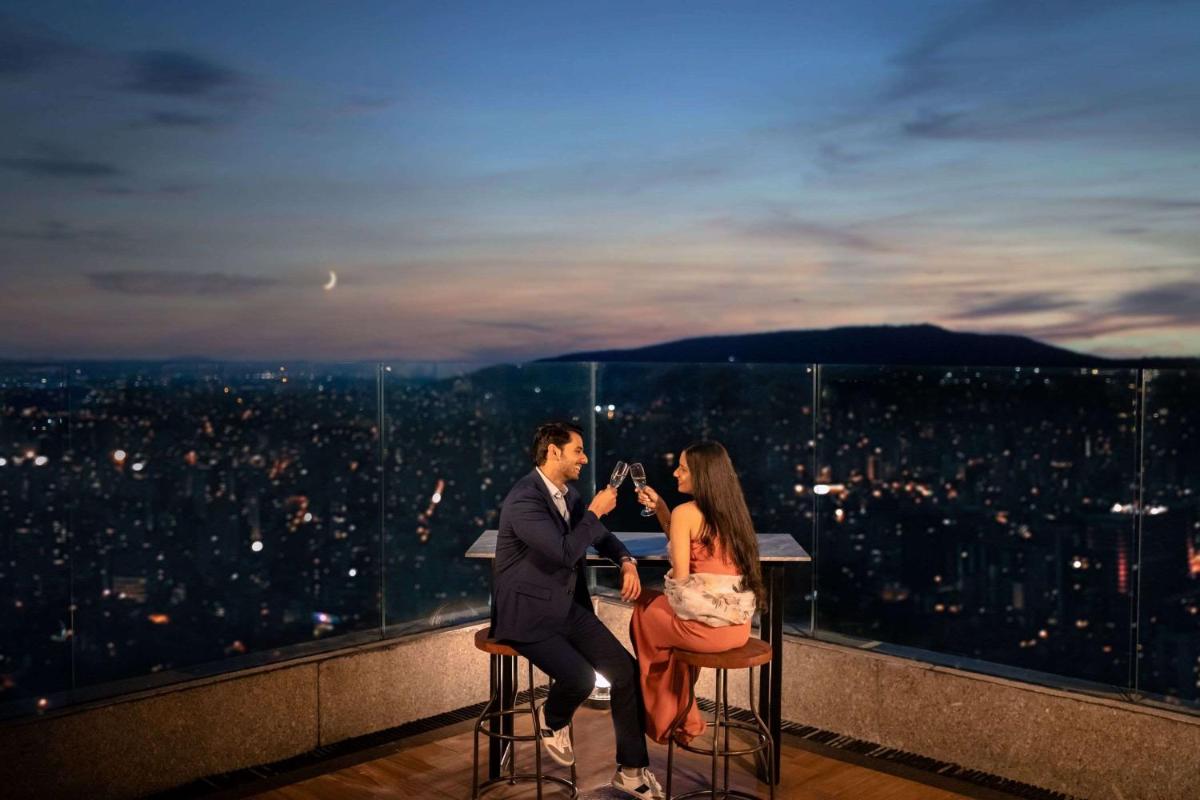 a man and a woman sitting on bar stools on the edge of a city at Hyatt Regency Dehradun Resort and Spa in Dehradun