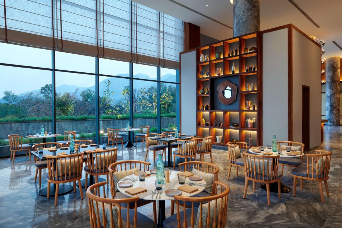 a restaurant with tables and chairs and large windows at Hyatt Regency Dehradun Resort and Spa in Dehradun