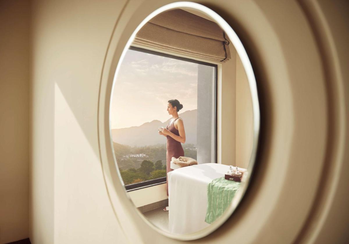 a woman looking out the window of a room with a table at Hyatt Regency Dehradun Resort and Spa in Dehradun
