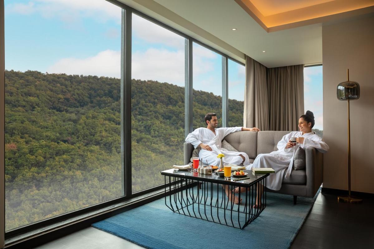 a man and woman sitting on a couch in a room with windows at Hyatt Regency Dehradun Resort and Spa in Dehradun