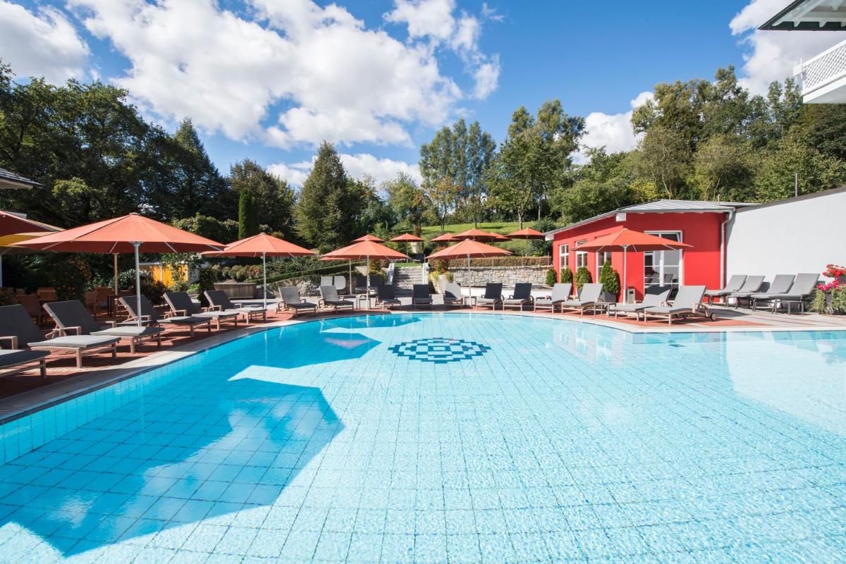 ein Pool in einem Hotel mit Stühlen und Sonnenschirmen in der Unterkunft Hotel St. Wolfgang in Bad Griesbach ein Pool in einem Hotel mit Stühlen und Sonnenschirmen in der Unterkunft Hotel St. Wolfgang in Bad Griesbach