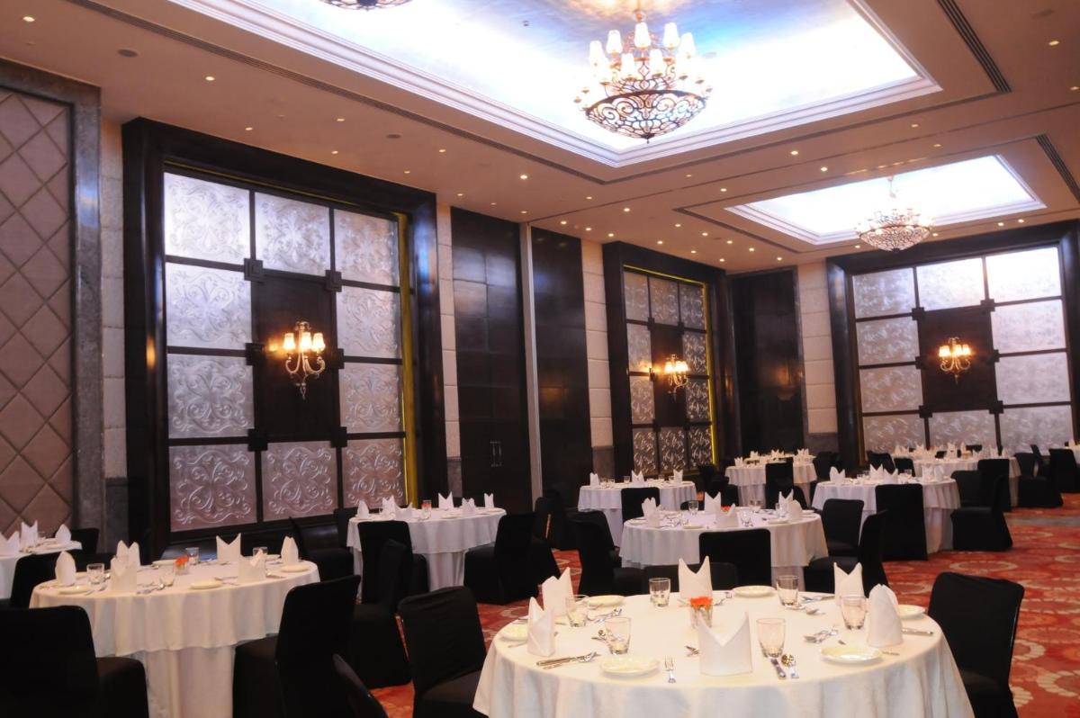 a banquet hall with white tables and chairs and chandeliers at The Pllazio Hotel in Gurgaon