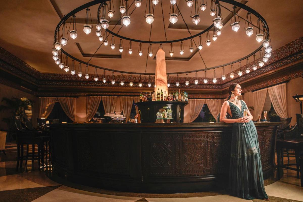 a woman standing in front of a bar with a chandelier at Fairmont Jaipur in Jaipur