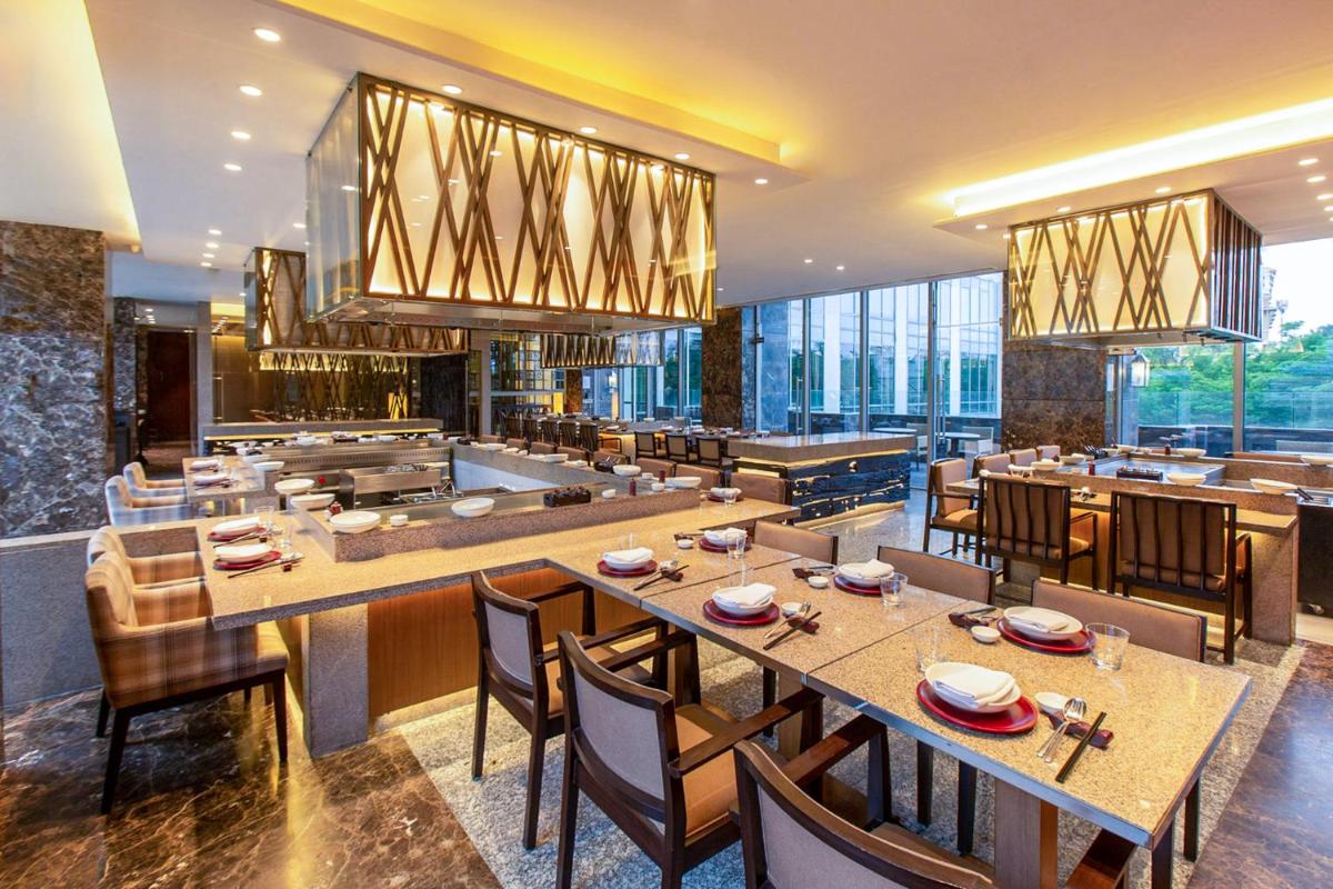 a restaurant with tables and chairs and a kitchen at Hyatt Ahmedabad in Ahmedabad