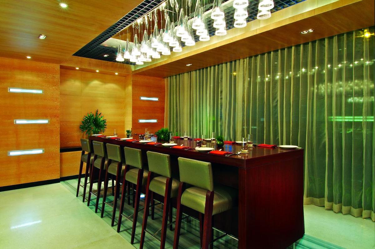 a restaurant with a long bar with chairs and lights at Vivanta Hyderabad, Begumpet in Hyderabad a restaurant with a long bar with chairs and lights at Vivanta Hyderabad, Begumpet in Hyderabad