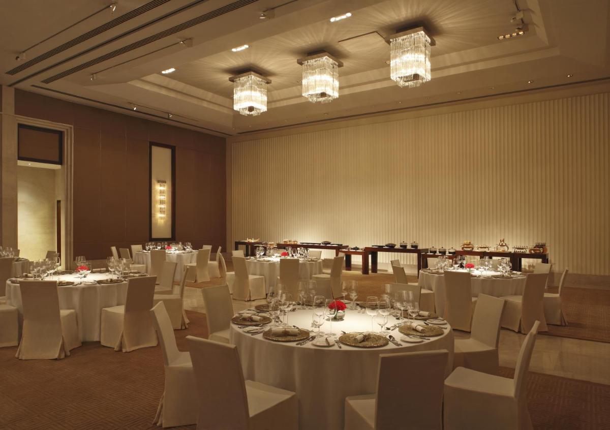 a banquet hall with white tables and chairs and chandeliers at The Oberoi Gurgaon in Gurgaon