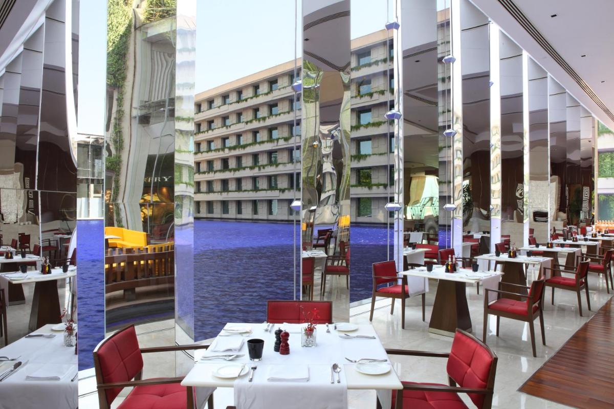 a restaurant with white tables and red chairs and a pool at The Oberoi Gurgaon in Gurgaon