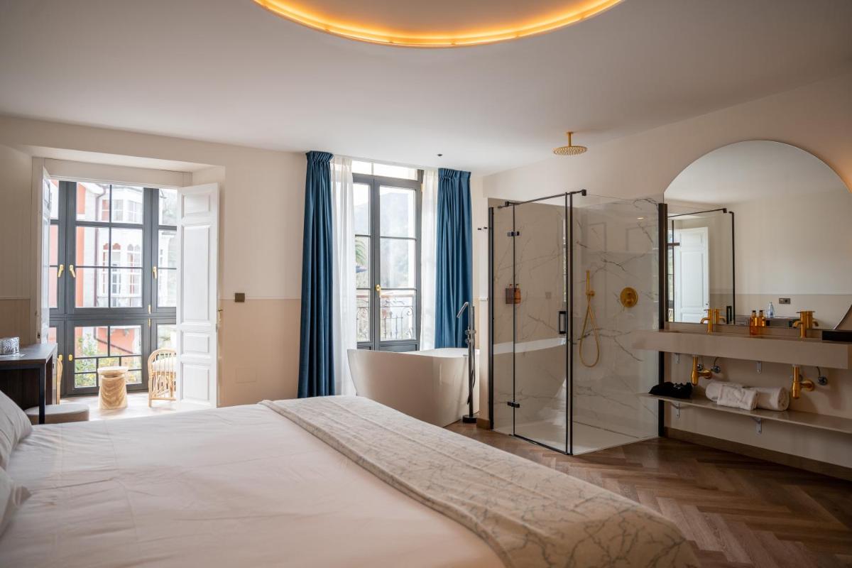 1 dormitorio con 1 cama grande y baño con ducha en Hotel Boutique Las Indianas, en Nueva de Llanes