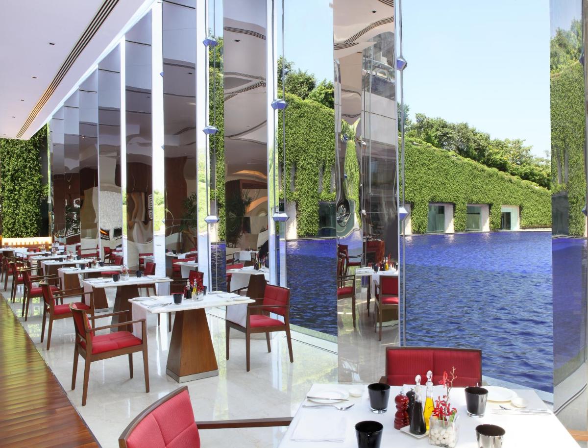 a restaurant with a pool and tables and chairs at The Oberoi Gurgaon in Gurgaon