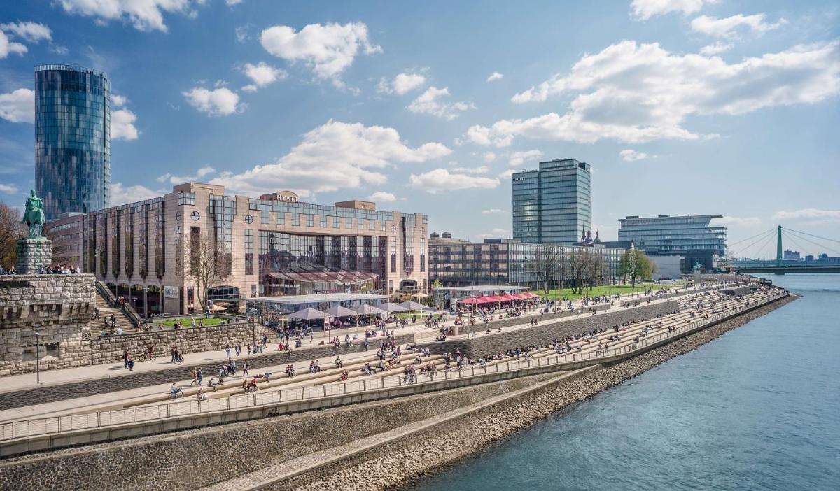 eine Gruppe von Menschen, die auf einem Bürgersteig neben dem Wasser spazieren in der Unterkunft Hyatt Regency Köln in Köln eine Gruppe von Menschen, die auf einem Bürgersteig neben dem Wasser spazieren in der Unterkunft Hyatt Regency Köln in Köln