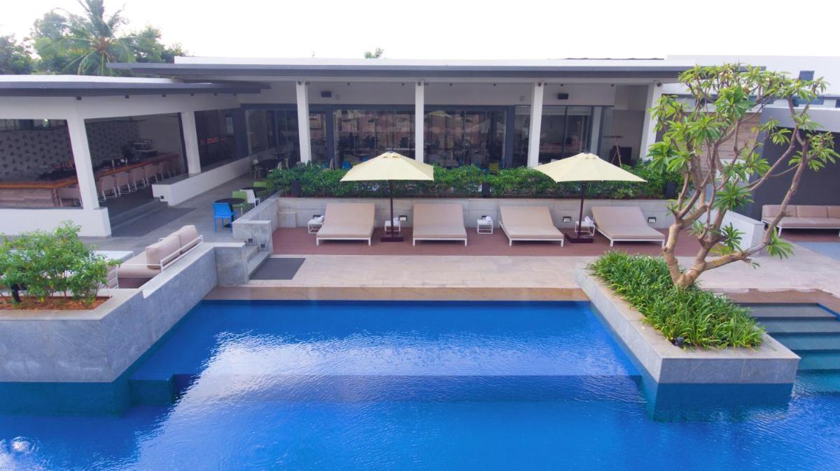 a swimming pool in front of a hotel with chairs and umbrellas at BLVD Club - Near BENGALURU AIRPORT in Bengaluru