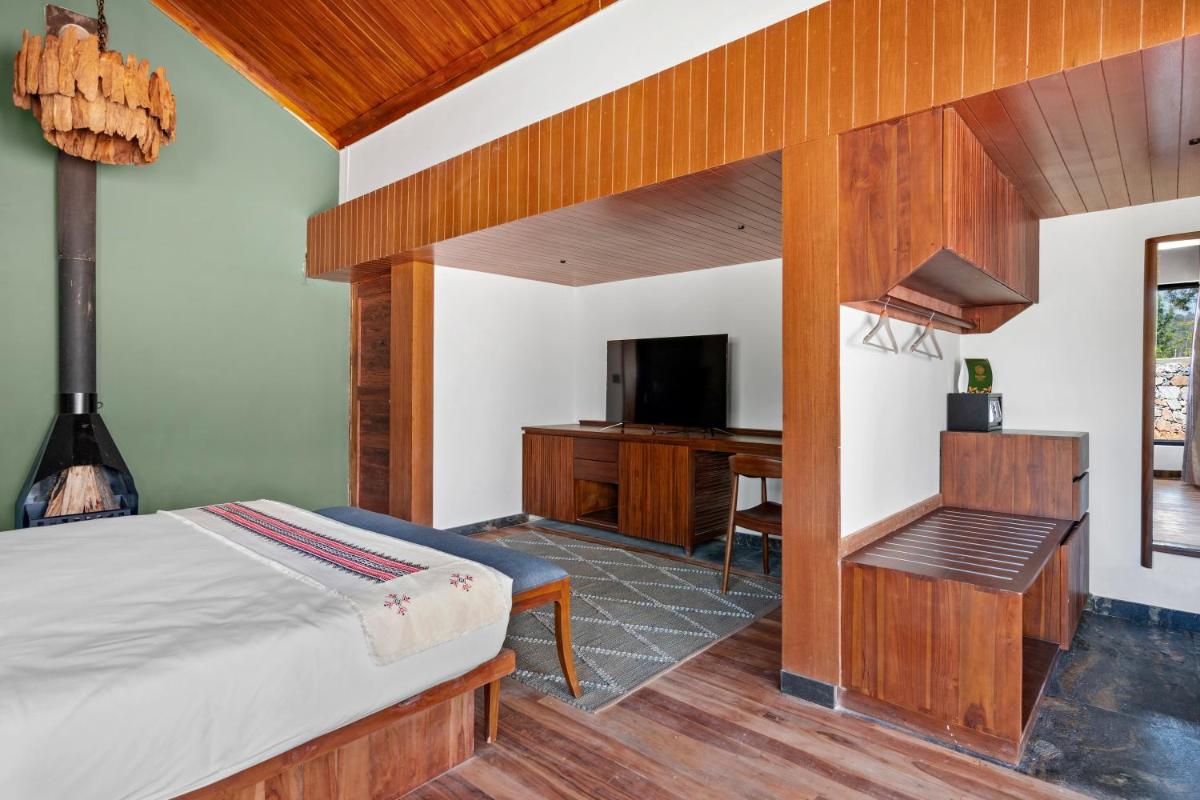 a bedroom with a bed and a desk and a television at WelcomHeritage Ayatana Ooty in Ooty