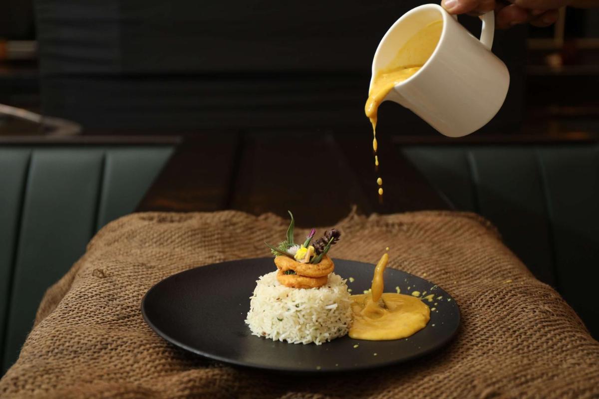 a plate of food on a table with a person pouring food at Hyatt Regency Amritsar Hotel & Spa in Amritsar