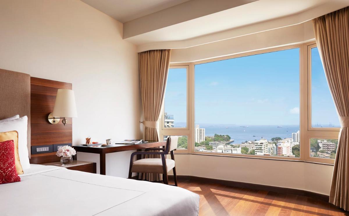 a hotel room with a bed and a desk and a large window at President - IHCL SeleQtions in Mumbai
