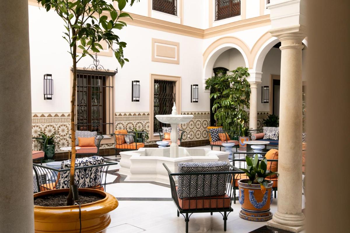 Un vestíbulo con mesas y sillas y un árbol. en Hotel Casa Palacio Don Ramón, en Sevilla