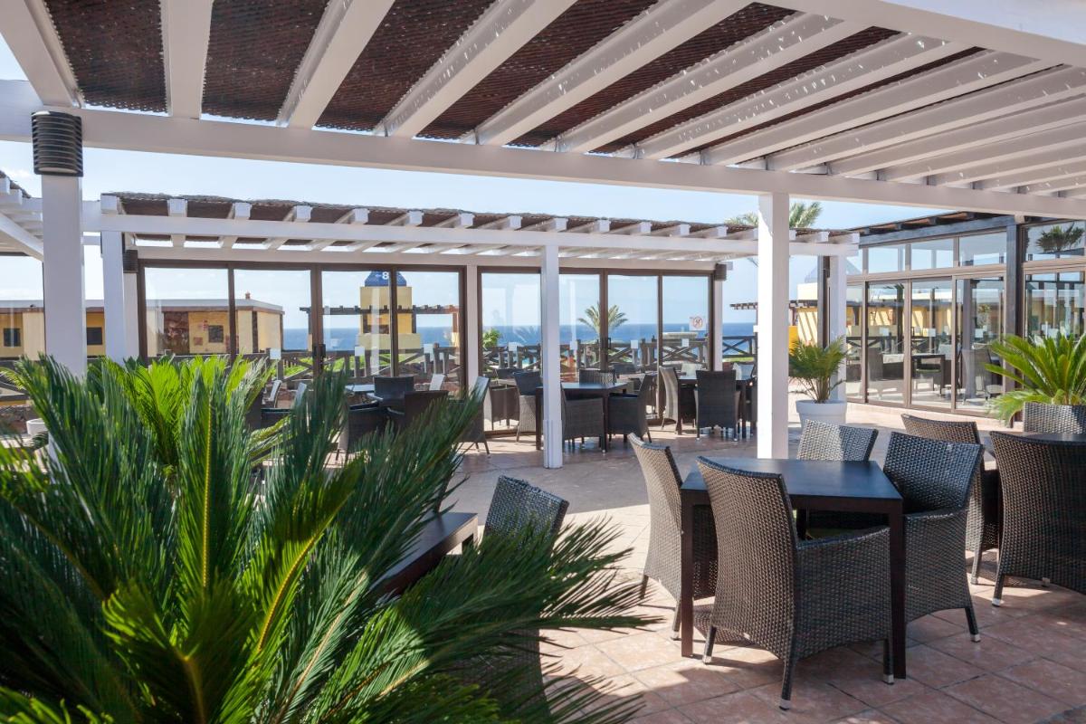Un patio al aire libre con mesas y sillas y una pérgola. en Occidental Jandía Playa, en Morro del Jable