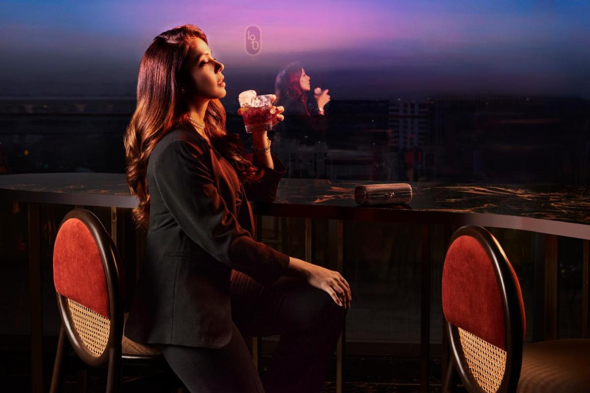 a woman sitting at a table drinking a drink at Novotel Mumbai International Airport in Mumbai
